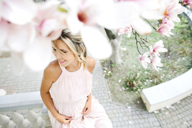 Lächelnde blonde Frau im Kleid, das unter dem Baum sitzt