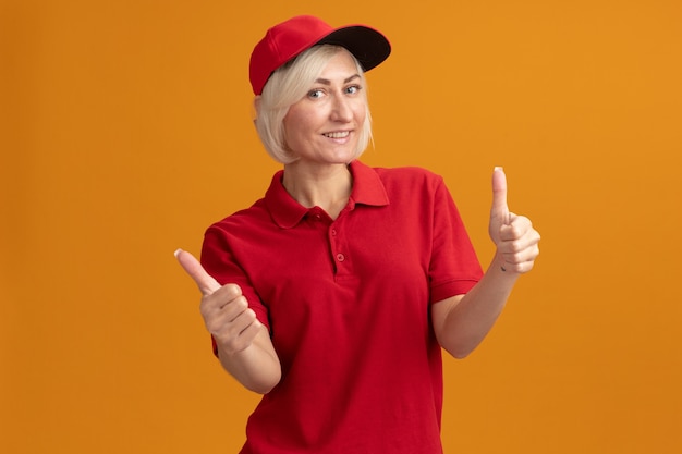 Lächelnde blonde Lieferfrau mittleren Alters in roter Uniform und Mütze mit Daumen nach oben