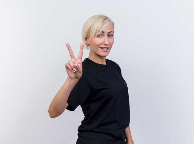 Lächelnde blonde slawische Frau mittleren Alters, die Friedenszeichen betrachtet Kamera betrachtet auf weißem Hintergrund mit Kopienraum