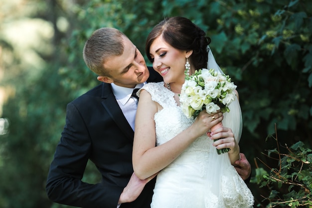 Lächelnde Braut mit dem Bräutigam und einem schönen Blumenstrauß
