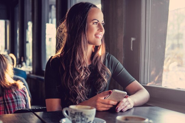 Lächelnde Brünette Frau mit einem Smartphone in einem Café.