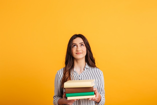 Lächelnde Brunettefrau im Hemd, das Bücher hält und oben schaut