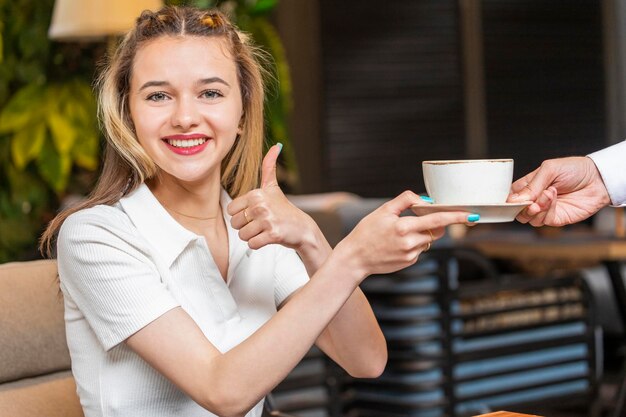 Lächelnde Dame, die Kaffee vom Kellner nimmt und mit dem Daumen nach oben gestikuliert