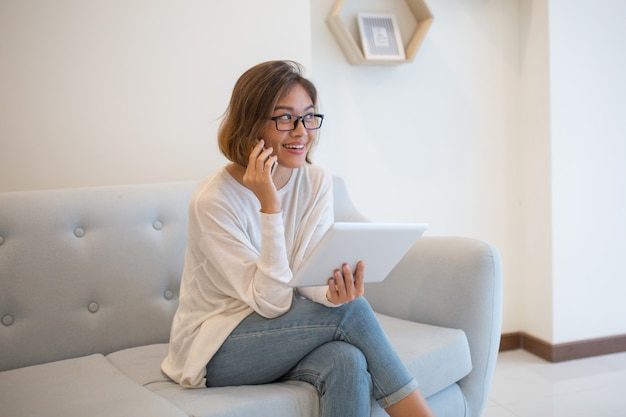 Lächelnde Dame, die Tablette hält und zu Hause am Telefon spricht