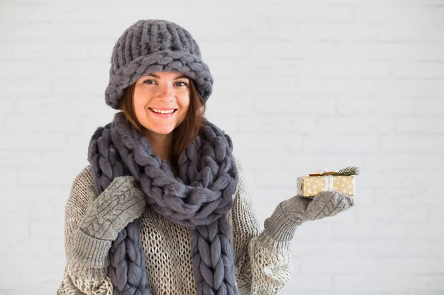 Lächelnde Dame in Handschuhen, Mütze und Schal mit Präsentkarton