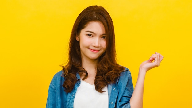 Lächelnde entzückende asiatische Frau mit positivem Ausdruck, lächelt breit, gekleidet in Freizeitkleidung und schaut in die Kamera über gelber Wand. Glückliche entzückende frohe Frau freut sich über Erfolg.