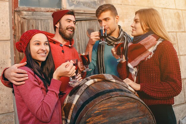 Lächelnde europäische Männer und Frauen während des Party-Fotoshootings. Die Jungs posieren als Freunde beim Studiofest mit Weingläsern mit heißem Glühwein im Vordergrund.