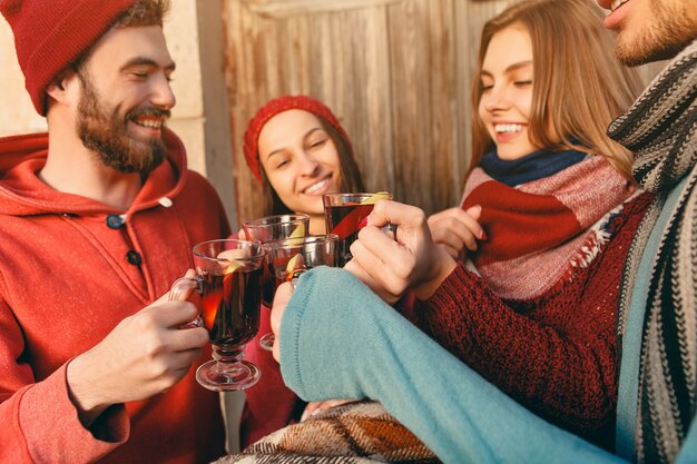 Lächelnde europäische Männer und Frauen während des Party-Fotoshootings. Jungs posieren als Freunde beim Studiofest mit Weingläsern mit heißem Glühwein im Vordergrund.