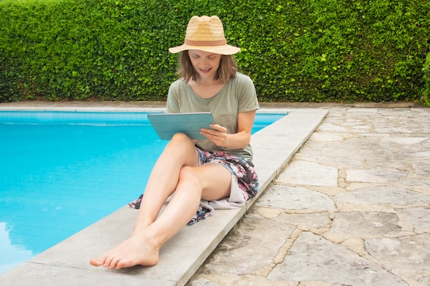 Lächelnde fokussierte Frau, die mit Tablette am Schwimmbad arbeitet