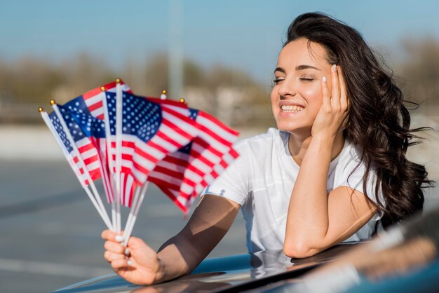 Lächelnde Frau des mittleren Schusses, die USA-Flaggen auf Auto hält