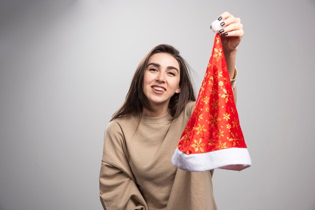 Lächelnde Frau, die an Santas Hut auf einem grauen Hintergrund zeigt.