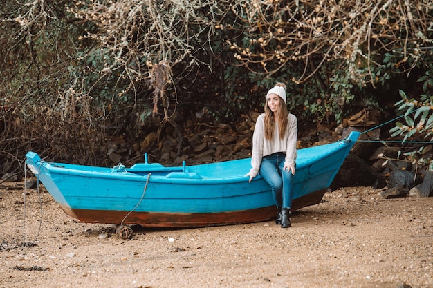 Lächelnde Frau, die auf einem Holzboot am Strand sitzt