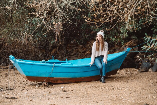 Lächelnde Frau, die auf einem Holzboot am Strand sitzt