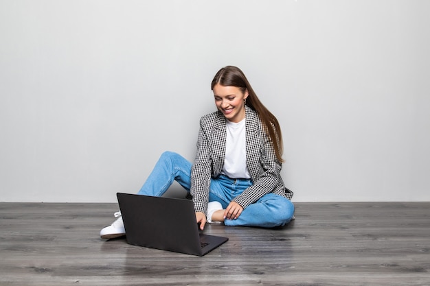 Lächelnde Frau, die auf Laptop-Computer tippt, während auf dem Boden mit gekreuzten Beinen isoliert sitzt