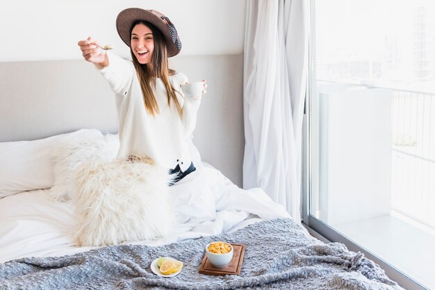 Lächelnde Frau, die das Frühstück sitzt auf dem Bett anbietet