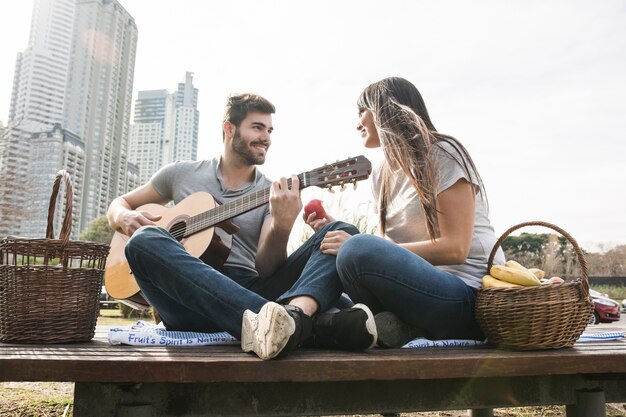 Lächelnde Frau, die den Mann spielt Gitarre Picknick betrachtet