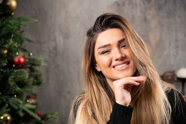 Lächelnde Frau, die die Kamera im gemütlichen Weihnachtsinnenraum betrachtet. Hochwertiges Foto