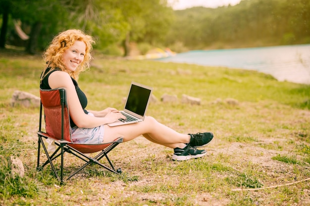 Lächelnde Frau, die draußen an Laptop arbeitet