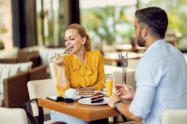 Lächelnde Frau, die ein Dessert genießt, während sie mit ihrem Freund in einem Café ist