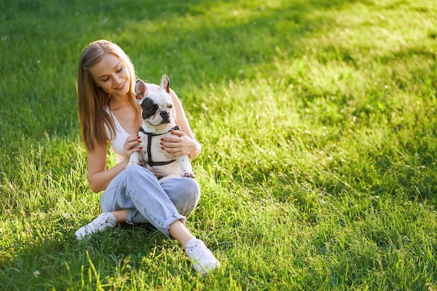 Lächelnde Frau, die französische Bulldogge auf Gras umarmt