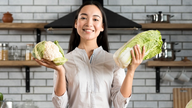 Kostenloses Foto lächelnde frau, die frischen grünen blumenkohl und kopfsalat in der küche zeigt