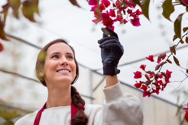 Lächelnde Frau, die Gartenkleidung trägt und Blumen im Gewächshaus bewundert