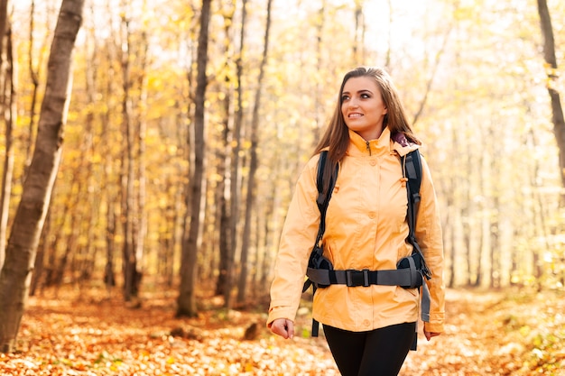 Lächelnde Frau, die gelbe Jacke trägt, die im Wald geht