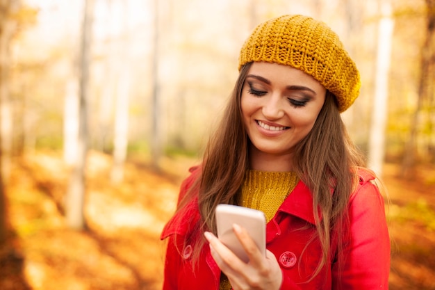 Lächelnde Frau, die Handy im Park während des Herbstes benutzt