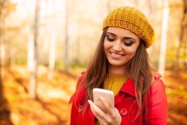 Lächelnde Frau, die Handy im Park während des Herbstes benutzt