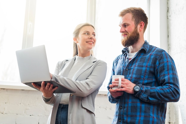 Lächelnde Frau, die ihrem Kollegen Laptop am Arbeitsplatz zeigt