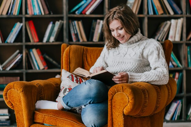 Lächelnde Frau, die im Lehnsessel liest