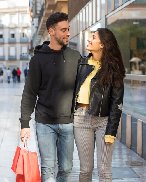 Lächelnde Frau, die jungen positiven Mann mit Einkaufspaketen umarmt