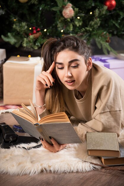 Lächelnde Frau, die sich auf einem flauschigen Teppich hinlegt und ein Buch liest.