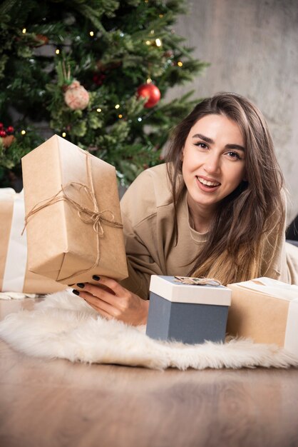Lächelnde Frau, die sich auf flauschigem Teppich hinlegt und ein Weihnachtsgeschenk zeigt.