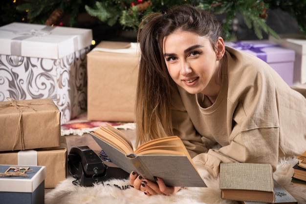 Lächelnde Frau, die sich auf flauschigen Teppich mit Büchern hinlegt.