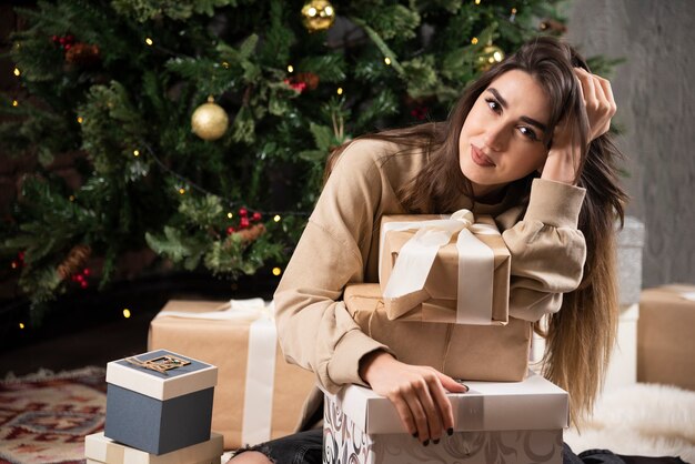 Lächelnde Frau, die sich auf flauschigen Teppich mit Weihnachtsgeschenken hinlegt.