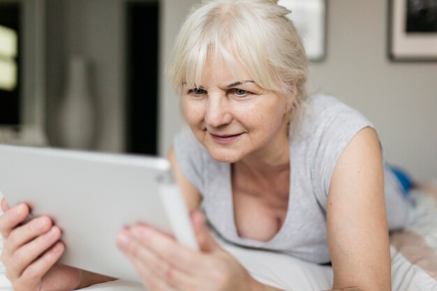 Lächelnde Frau, die Tablette auf Bett durchstöbert