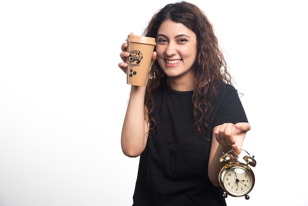 Lächelnde Frau, die Tasse Kaffee mit Uhr auf weißem Hintergrund zeigt. Hochwertiges Foto