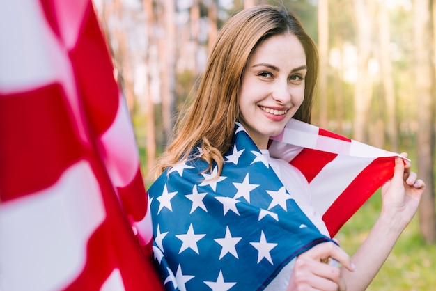 Lächelnde Frau eingewickelt in der nationalen amerikanischen Flagge