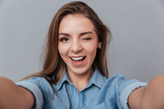 Lächelnde Frau im Hemd, das Selfie im Studio macht und zwinkert