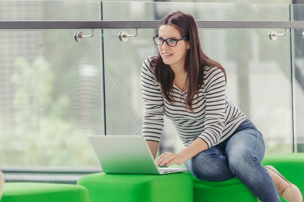 Lächelnde Frau in den Schauspielen unter Verwendung des Laptops