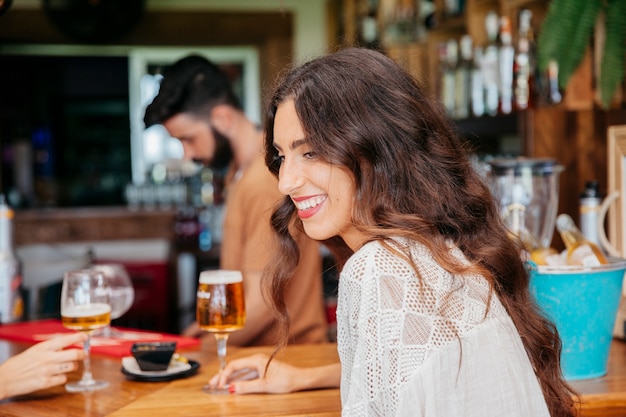 Lächelnde Frau mit Bier sitzt in bar