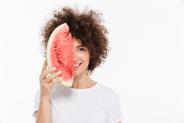 Lächelnde Frau mit dem lockigen Haar, das Scheibe einer Wassermelone hält