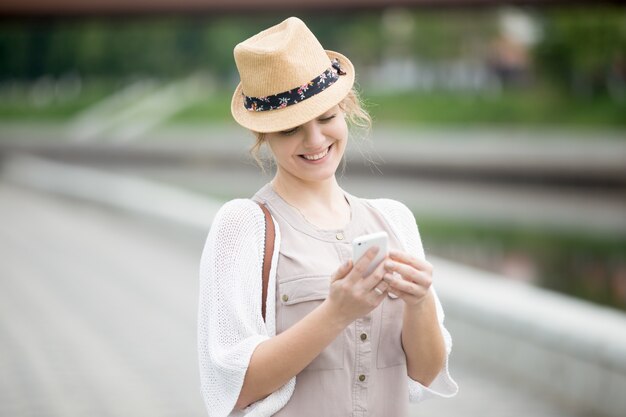 Lächelnde Frau mit Hut auf ihrem Handy suchen