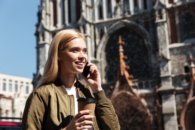 Lächelnde Frau mit Kaffee, der auf Smartphone spricht