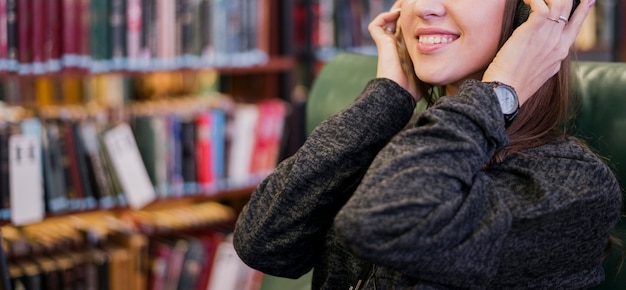 Lächelnde Frau mit Kopfhörern nähern sich Bücherregal