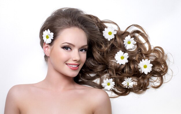 Lächelnde Frau mit schönen langen Haaren wna Blumen darin auf Weiß