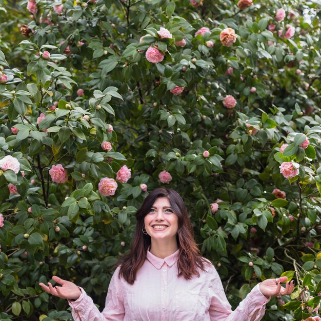 Lächelnde Frau nahe den rosa Blumen, die auf grünen Zweigen wachsen