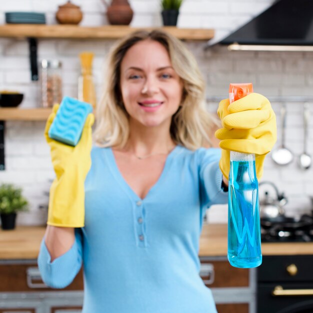 Lächelnde Frau, welche die Gummihandschuhe halten Reinigungsmittel mit Schwamm trägt