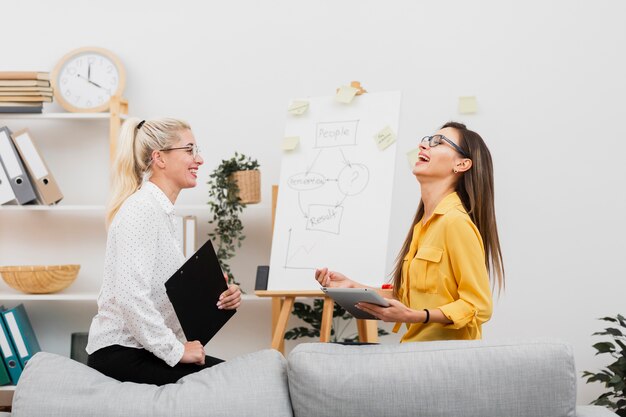 Lächelnde Frauen der Seitenansicht, die eine Tablette und ein Klemmbrett halten